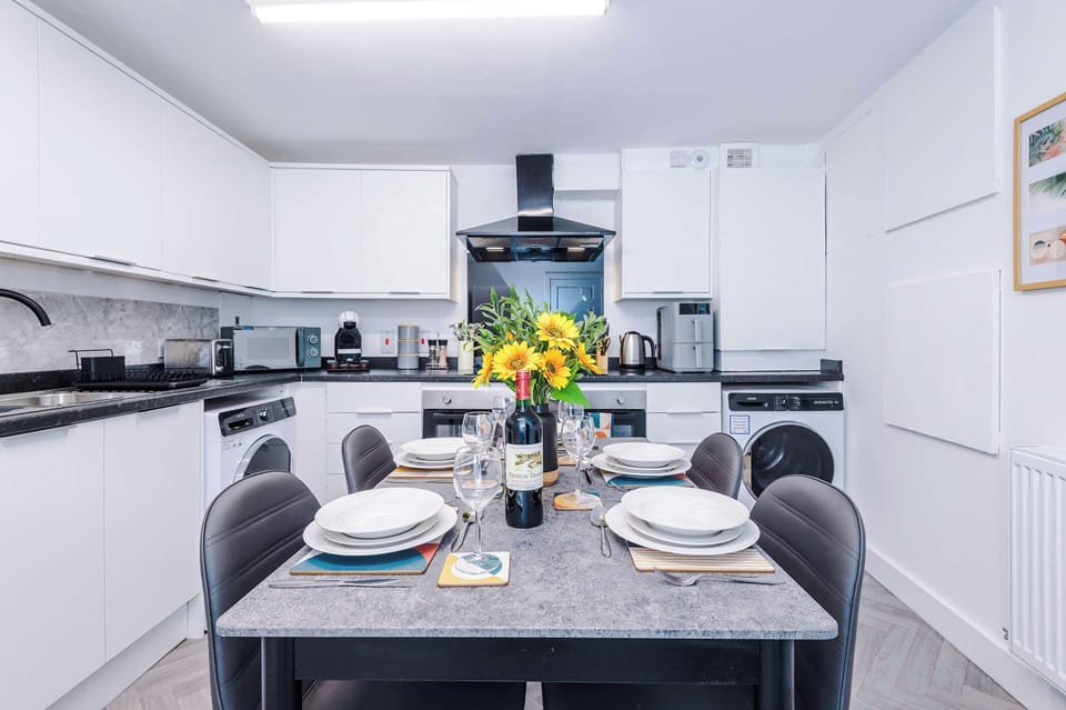 Bright, modern kitchen with a well-planned layout with integrated oven, hob with extractor, washing machine, and generous worktop space. The dining table with seating sits neatly within the room.