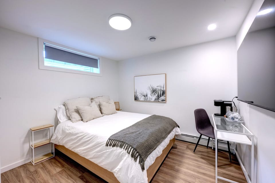 Bright second bedroom with queen bed, desk, and natural light from the above-grade window.