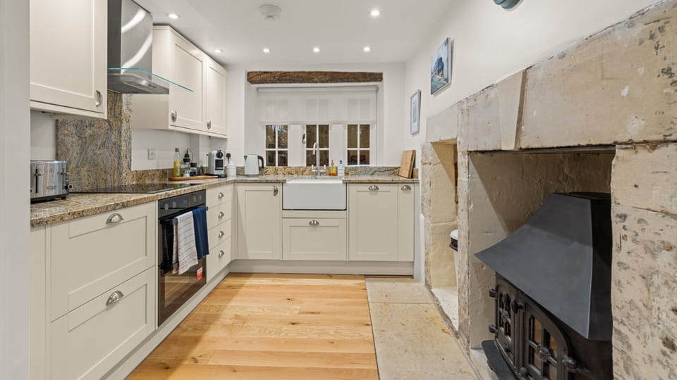 The kitchen is a timeless cottage-style space, featuring a Belfast sink set beneath the original window.