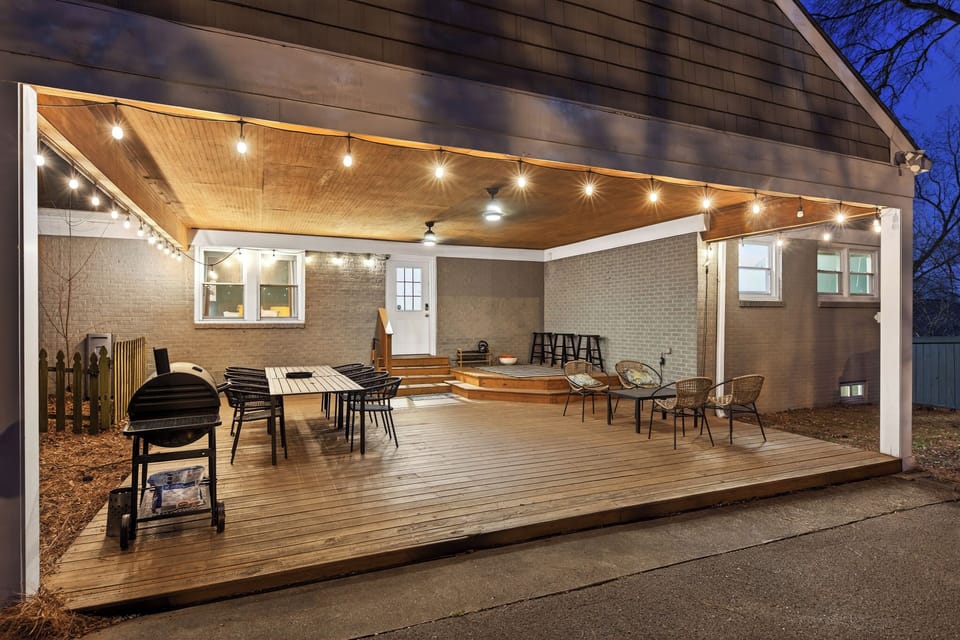 Covered outdoor deck with dining, lounge seating, string lights, and grill.