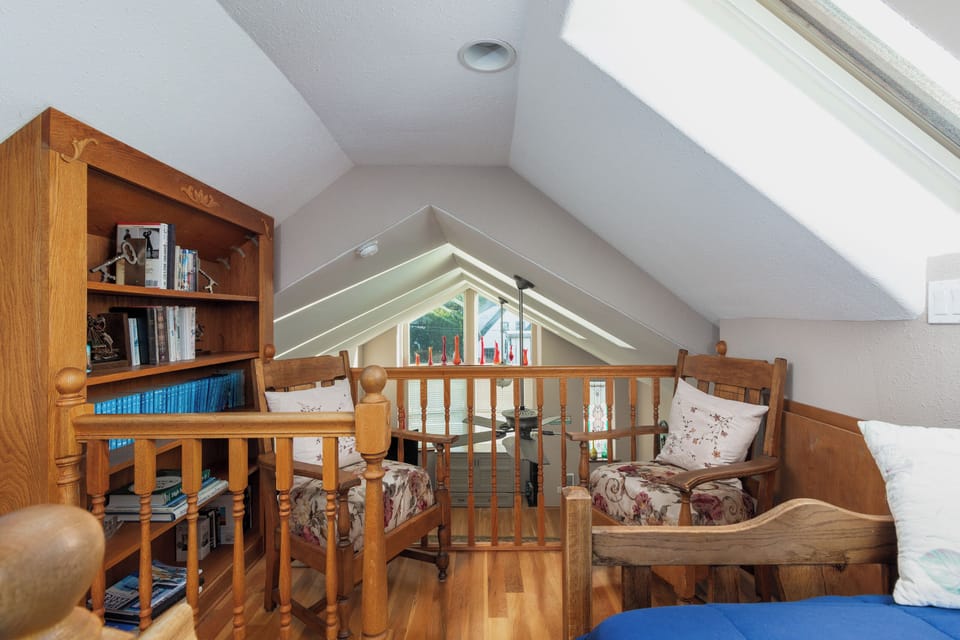 Cozy attic reading nook with warm wood furnishings, books, and natural light streaming through skylights.