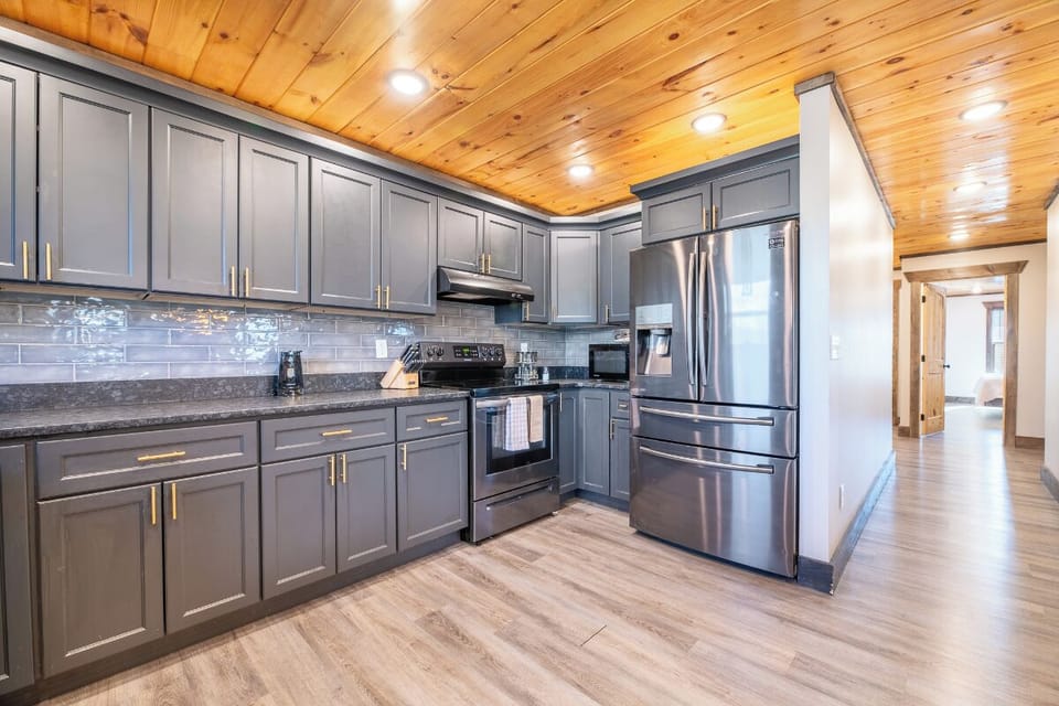 Your fully equipped kitchen features stainless steel appliances and elegant gray cabinets under rustic wood ceilings.