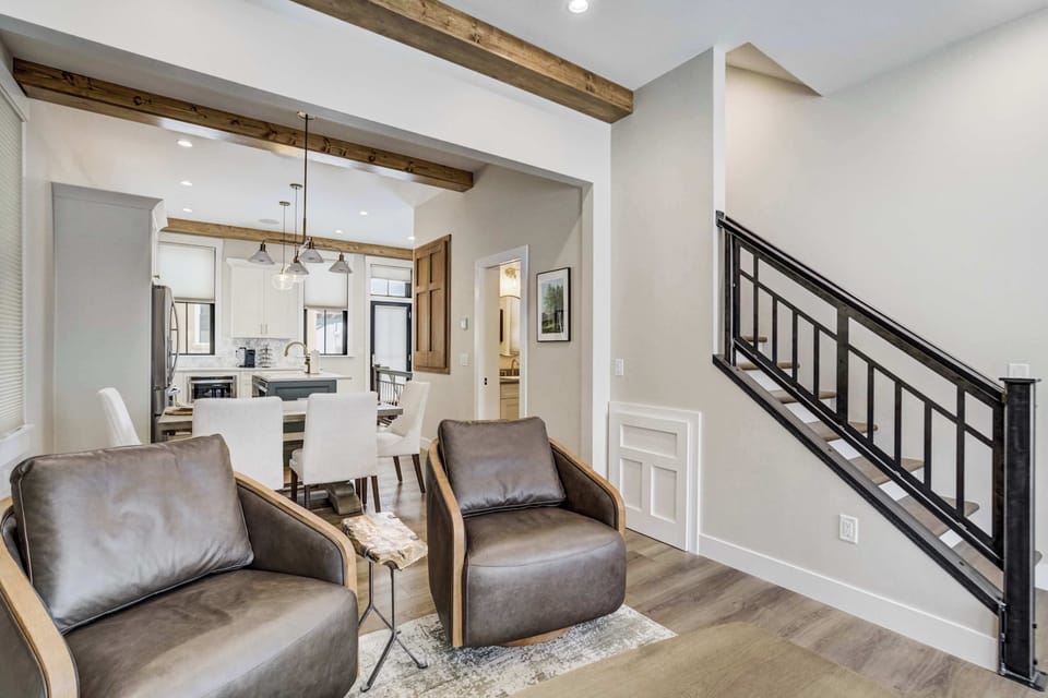 This open layout offers a seamless transition from the living area toward the dining space and kitchen. Stylish leather seating and light wood floors are framed by a modern staircase with clean black metal railings for a contemporary look.