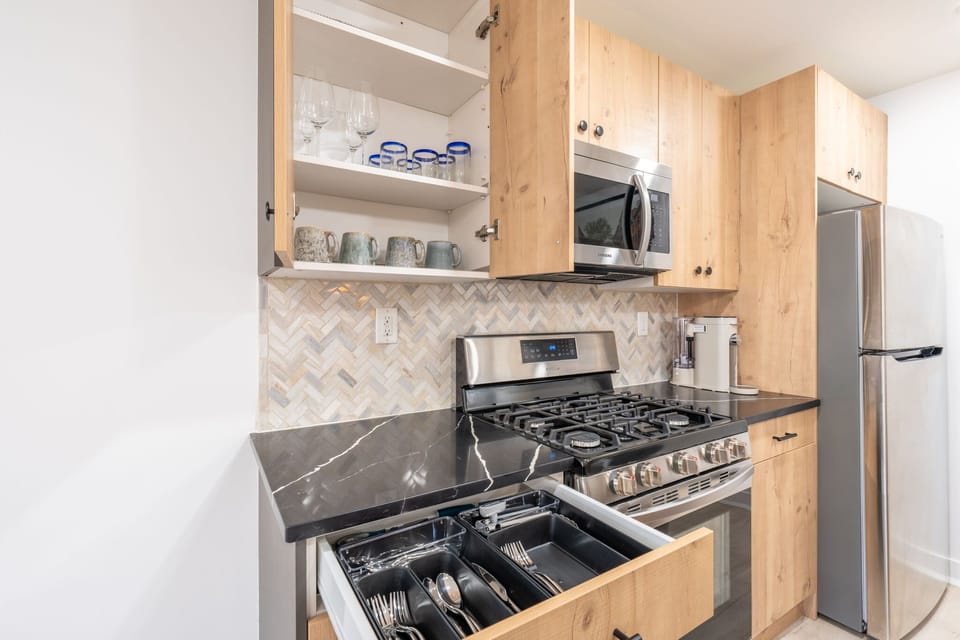 A well-equipped kitchen with a gas range and organized drawers for cutlery. The dark stone countertops offer plenty of space for food prep.