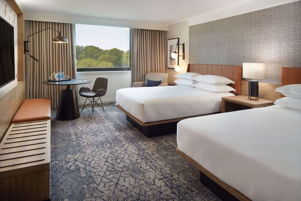 Room with two beds, sitting area, large window, and carpet floor