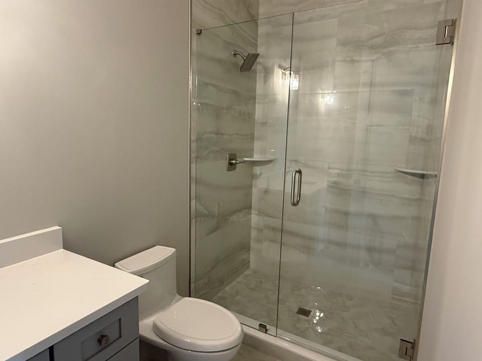 Step into your sleek glass-enclosed shower with modern marble-look tiles and rainfall showerhead for a luxurious daily routine.