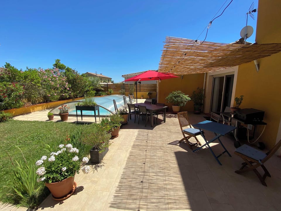 Terrasse avec parasol rouge, mobilier d'extérieur et façade de la villa