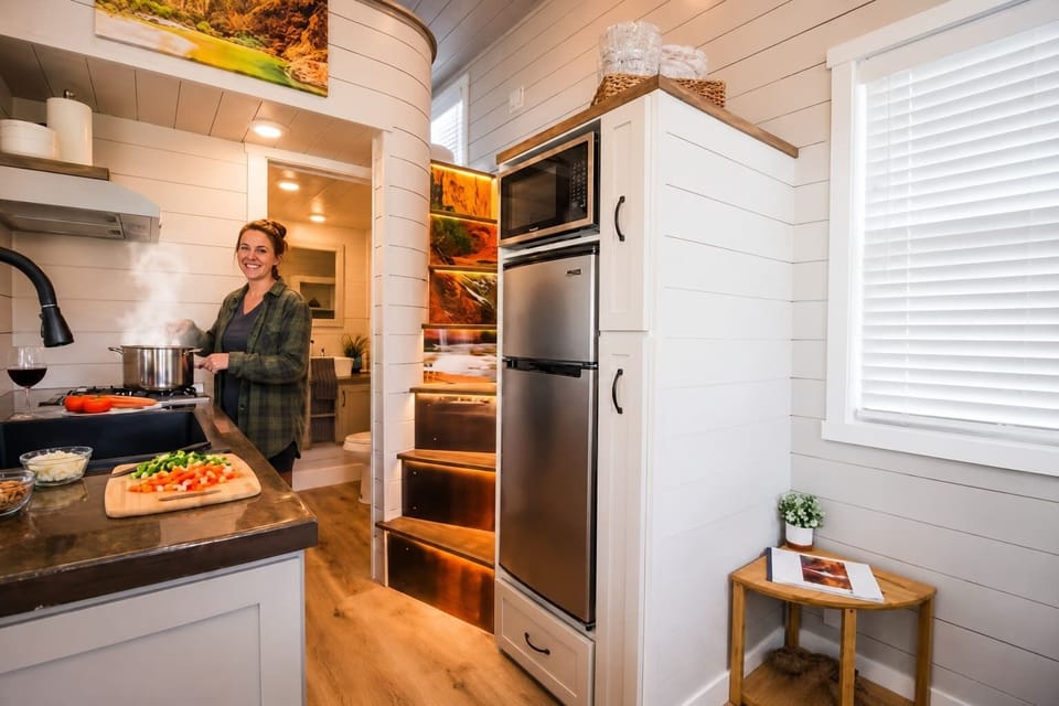 Bright, fully equipped kitchen with modern appliances, spacious countertops, cookware, and everything needed to prepare meals. Open layout with custom illuminated staircase leading to the loft bedroom in this cozy tiny home near Zion National Park.