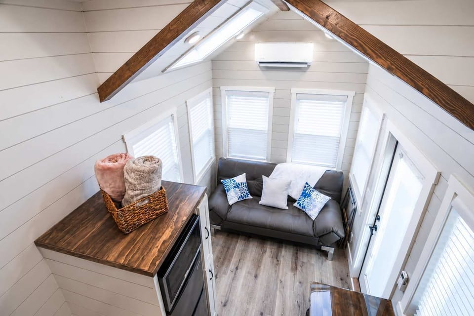 Bright, open-concept living area with comfortable charcoal sofa, vaulted ceilings, skylight, and large windows that fill the tiny home with natural light. Relax after exploring Zion National Park in this inviting gathering space.