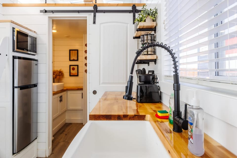 Open-concept tiny home kitchen with refrigerator, microwave, and cooktop, offering efficient use of space and easy flow throughout the home.