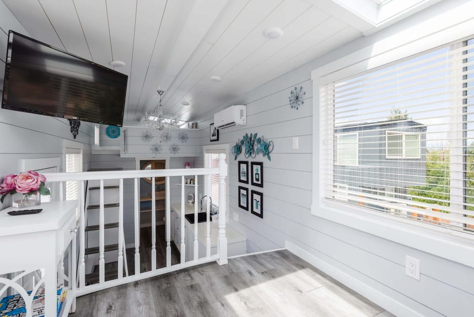 Inviting upper living space with a TV, large windows, and an open view across the tiny home for a bright and spacious feel.