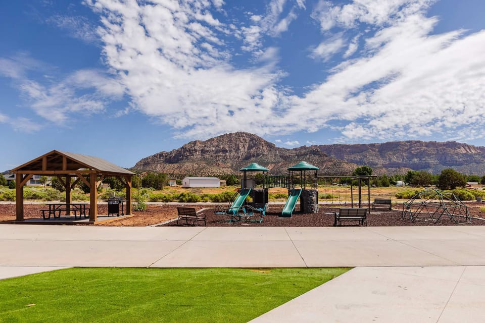 Family-friendly playground with slides, swings, a climbing dome, and an airplane teeter-totter. Benches nearby provide a comfortable place for parents to sit while kids enjoy outdoor play just steps from the tiny homes.