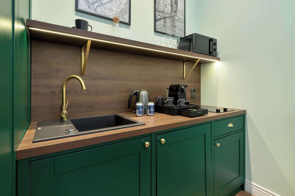 A compact kitchenette with dark green cabinets, a wooden countertop, and a stylish gold-colored sink faucet.