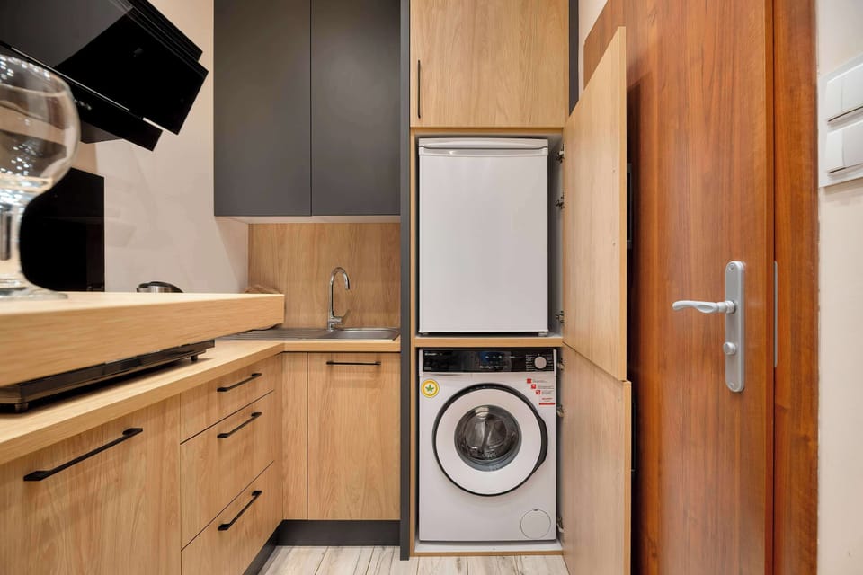 A compact kitchen area with a washing machine integrated into cabinetry. Wooden finishes unify the design. The space feels practical and modern.