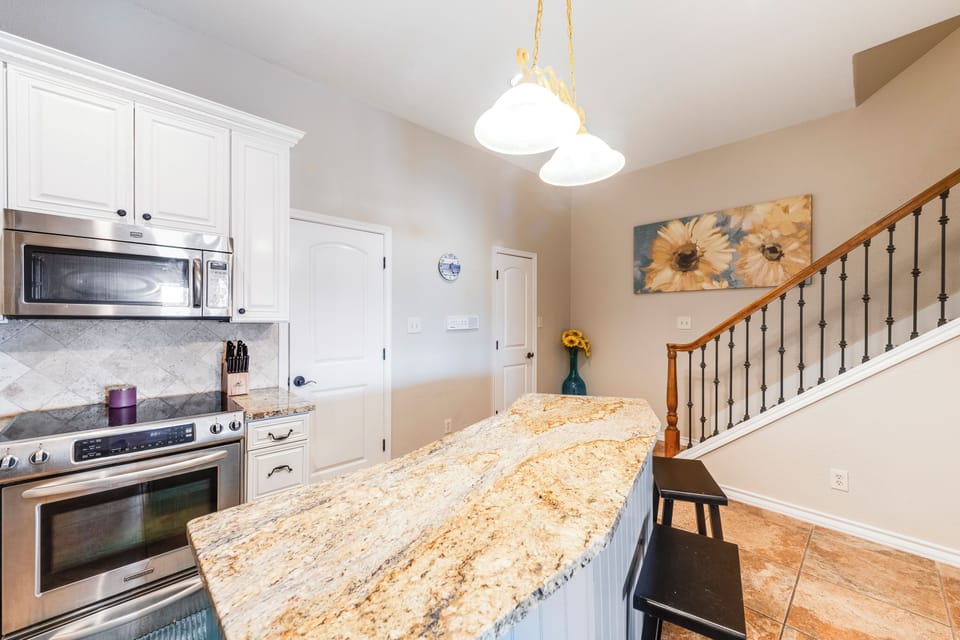 Your granite island anchors this elegant kitchen with white cabinetry and stainless appliances, perfect for morning coffee or evening meals together.