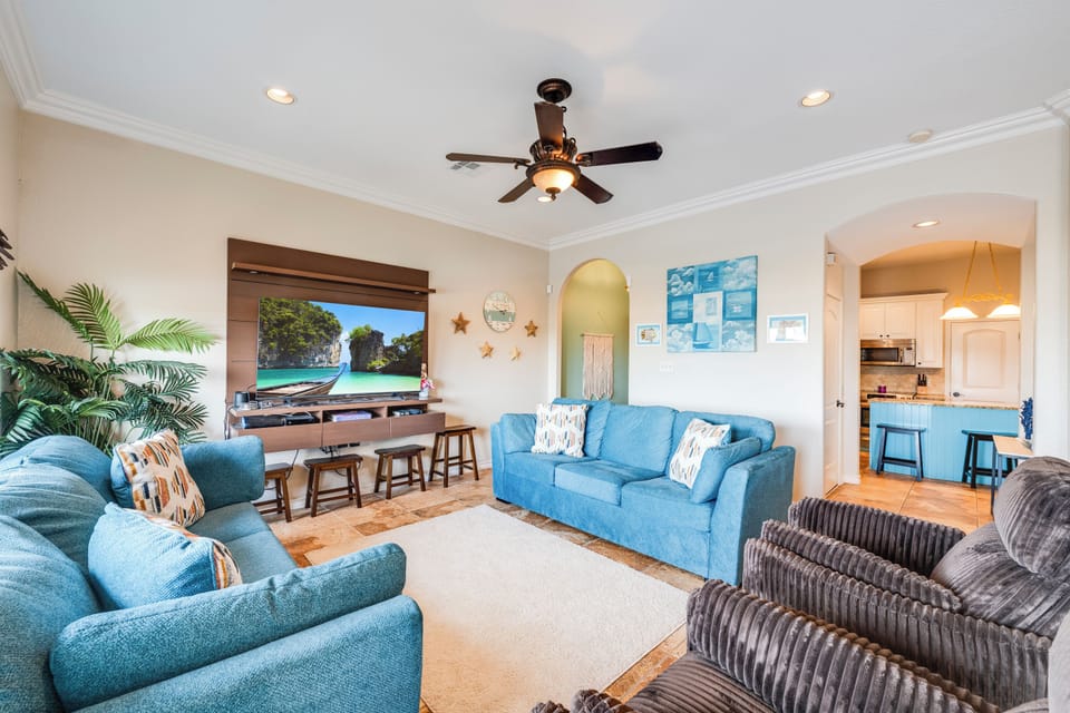 Unwind in your spacious living room with plush blue seating, tropical touches, and coastal artwork creating the perfect beach house atmosphere.