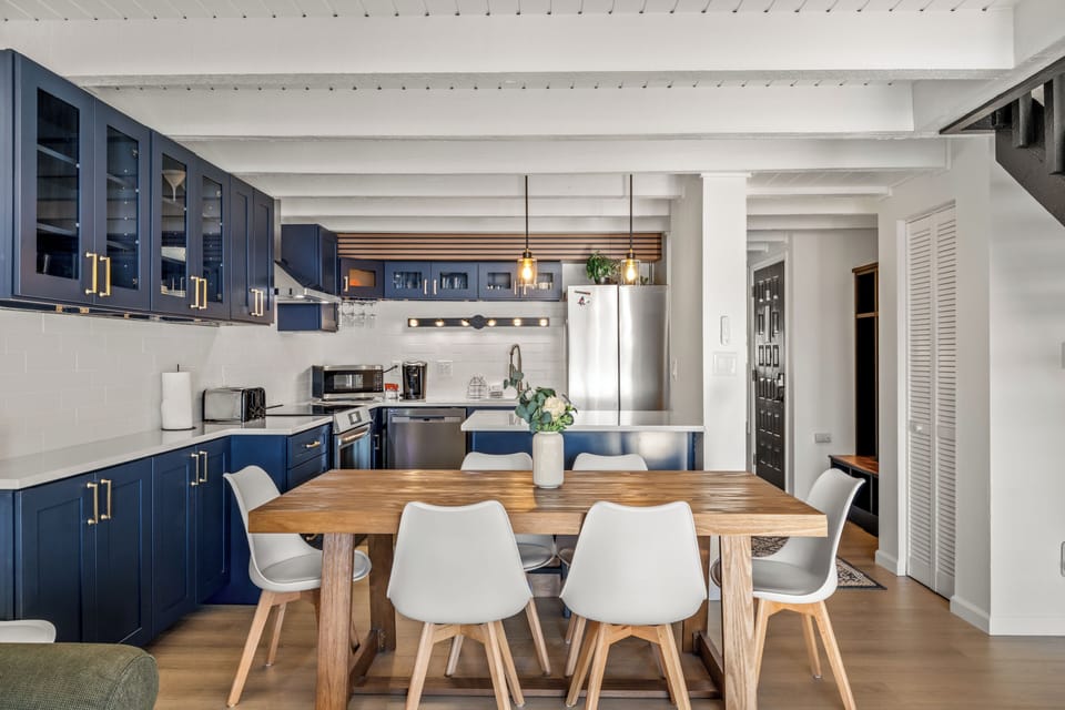 Your stunning open-plan kitchen features sleek navy cabinetry, modern appliances, and a warm wood dining table perfect for memorable meals.