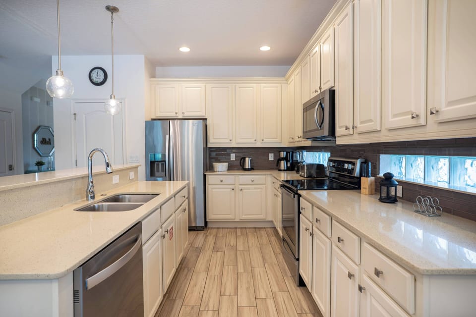 Welcome to this beautiful kitchen with sleek white cabinetry and a spacious quartz countertop, ideal for meal prep. The stainless steel appliances shine under warm lighting, making it an inviting space for your culinary creations.