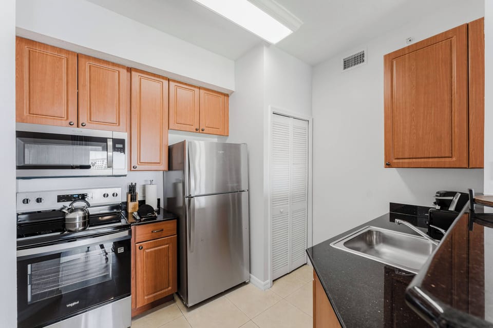 Enjoy a functional kitchen with rich wooden cabinets and sleek black countertops, complemented by stainless steel appliances. Bright lighting creates an inviting atmosphere, perfect for preparing delicious meals during your visit.