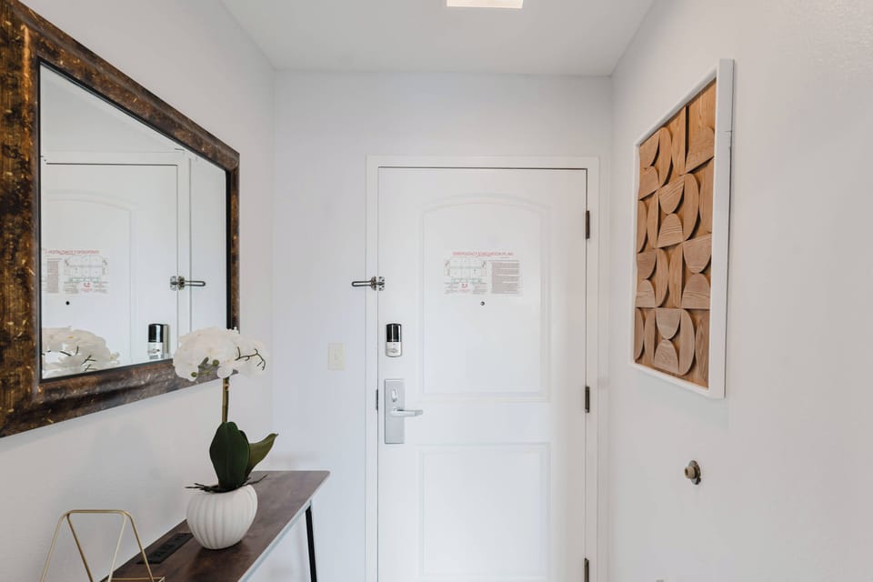 Enter a warm entryway featuring textured wall art that enhances the fresh white walls. A chic console table and sleek mirror reflect natural light, while a delicate orchid adds a lovely touch of nature to your space.