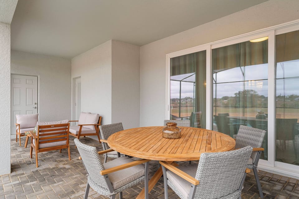 Relax on a covered patio with a round dining table, cozy outdoor seating, sliding glass doors, and peaceful green views, perfect for meals and family moments outside.