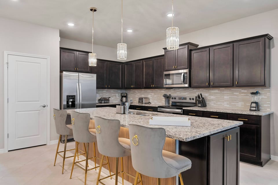 Cook and gather in a stylish fully equipped kitchen with dark cabinets, stainless steel appliances, granite countertops, elegant pendant lights, and a large island with seating, perfect for meals and family moments.