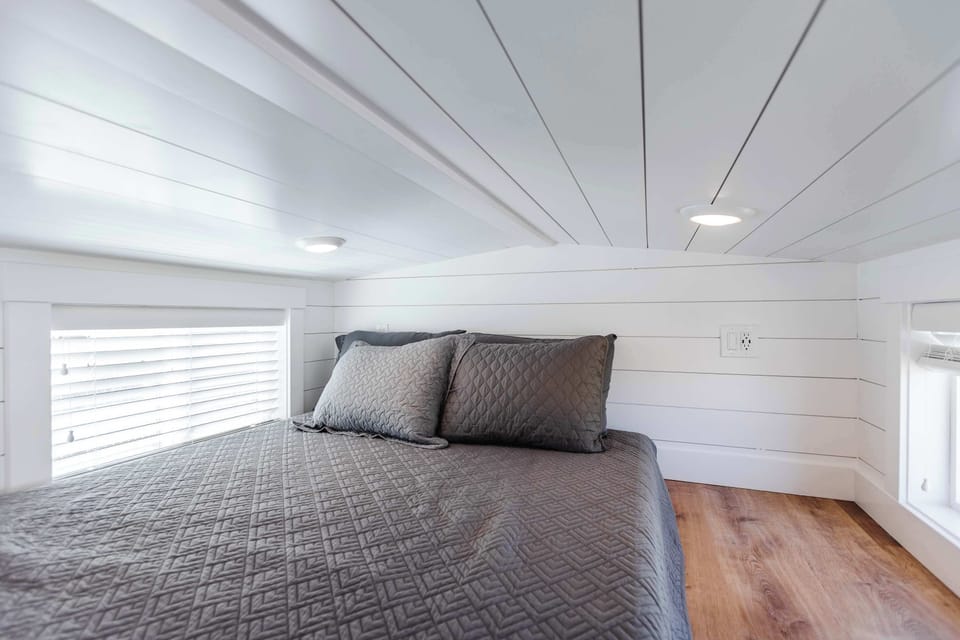 Cozy loft sleeping area with a queen bed, bright white interior, windows for natural light, and recessed lighting for a comfortable stay.