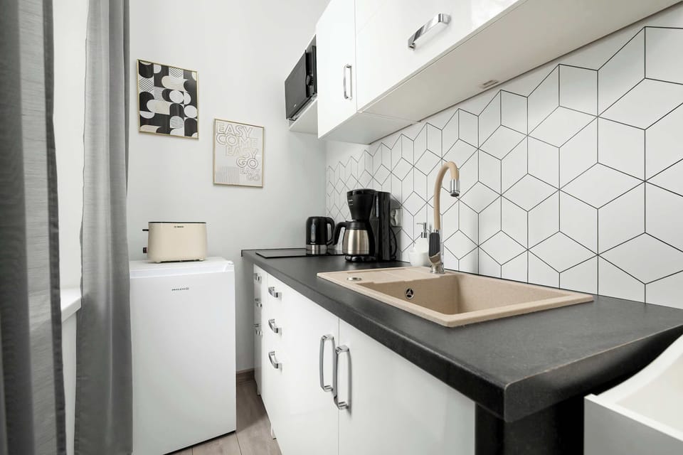 A modern kitchen with white cabinets, black countertops, and a tiled backsplash. Equipped with a coffee machine and sink, it’s practical for cooking.
