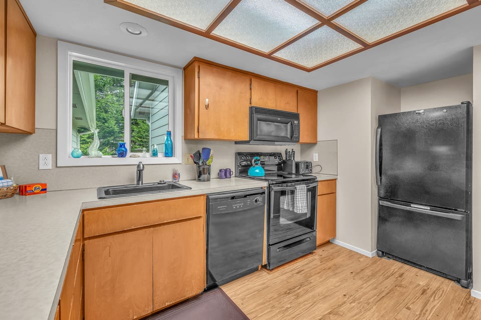 Your fully equipped kitchen features modern appliances, warm wood cabinetry, and a sunny window overlooking lush greenery for inspiring meal prep.