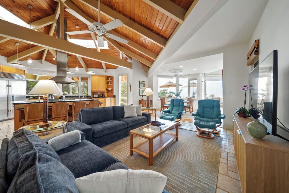 Relax in your spacious open-concept living area featuring soaring wood beam ceilings, comfortable seating, and seamless kitchen access.
