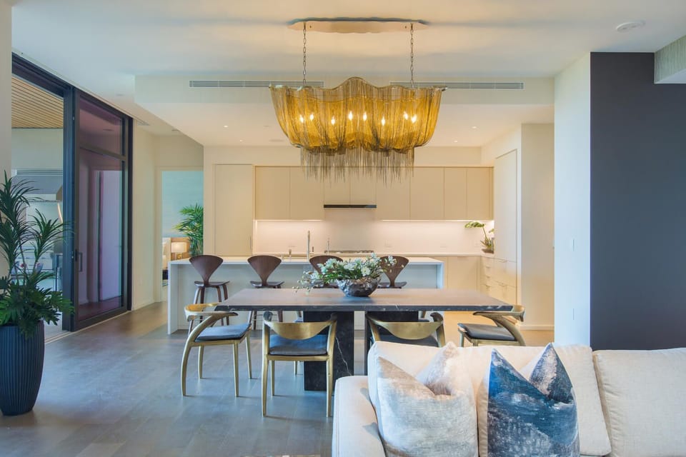 Step into your sophisticated open-plan space where golden light cascades from the stunning chandelier over your elegant dining table.
