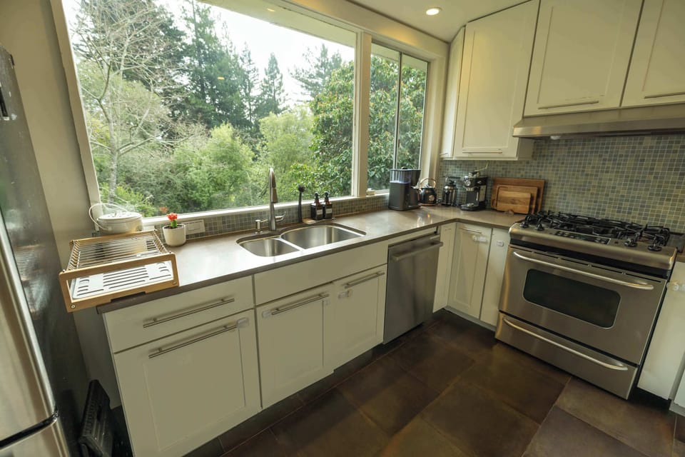 This sunlit kitchen with expansive windows, modern appliances, and generous counter space makes preparing meals effortless while enjoying peaceful greenery views