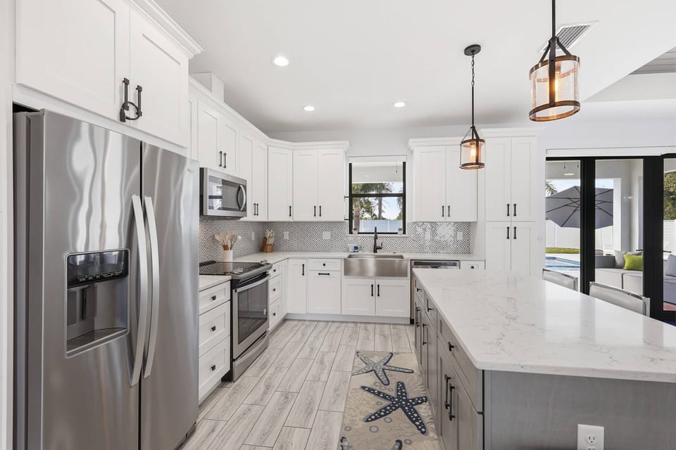 Well equipped with quartz counters, tiled backsplash, farmhouse sink, stainless steel appliances, and an island with bar stool seating.