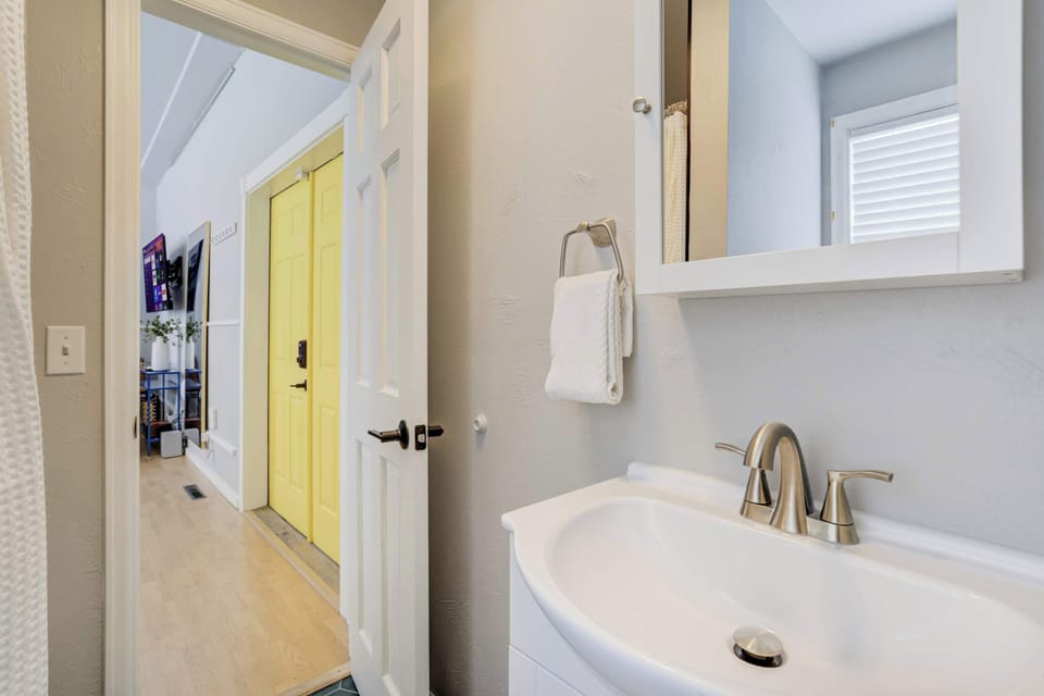 The thoughtfully designed bathroom features a modern white vanity with a sleek chrome faucet, offering a bright and clean space that maintains the studio's cohesive contemporary aesthetic and efficient use of space.