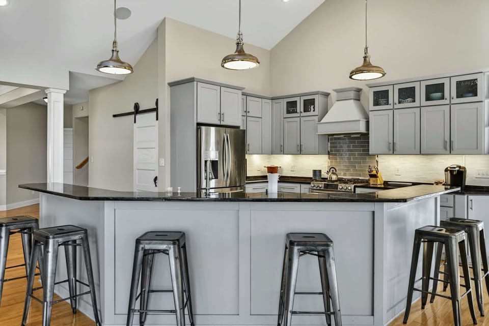 Kitchen - Gourmet kitchen with gray cabinetry, black granite island, industrial pendants, and bar seating for six.