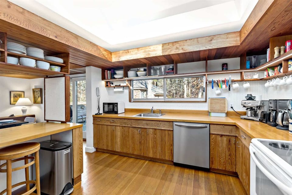 Fully equipped kitchen with plenty of counterspace, open shelving, and a window view into the trees for a true Cape Cod feel.