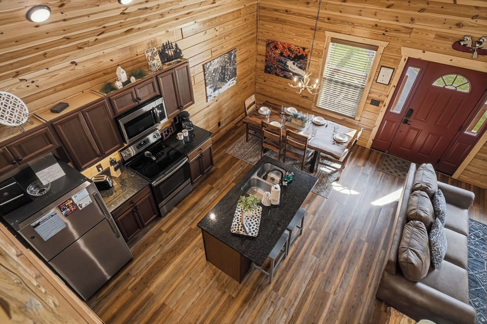 Your open-concept cabin retreat blends rustic warmth with modern comfort, where you'll cook in a fully-equipped kitchen, dine together, and relax on leather sofas under soaring wood-beamed ceilings.