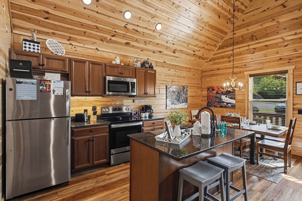 Your mountain retreat features a fully-equipped kitchen with granite counters, stainless appliances, and a cozy island—perfect for gathering over morning coffee or sharing meals surrounded by warm wood beams and natural light.