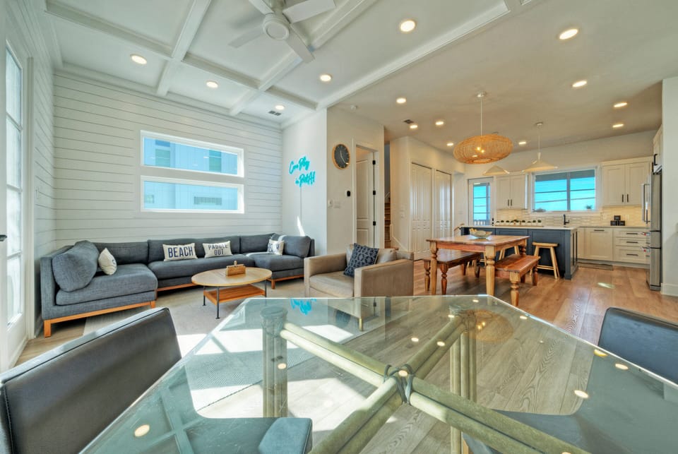 Sunlit living and dining space with balcony access, plush seating, and an open, coastal feel.