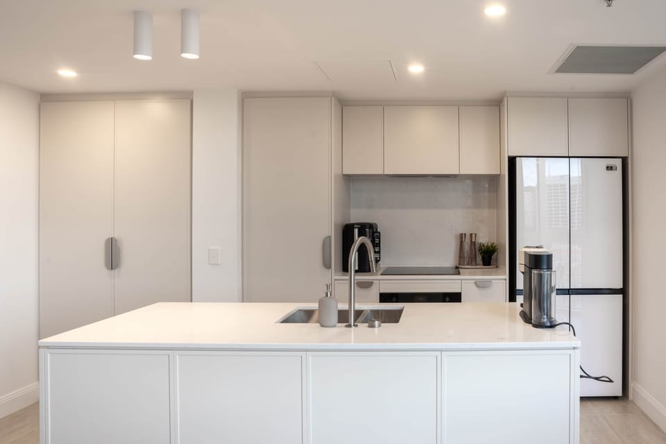 Sleek minimalist kitchen with spacious island and elegant glass-front fridge.