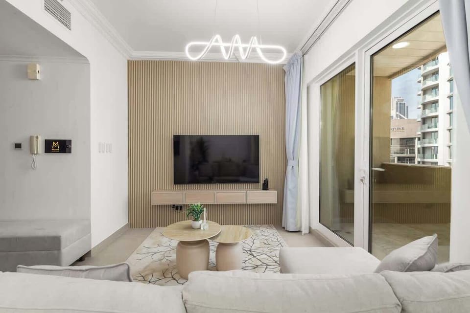 The smart home entertainment system takes center stage with a mounted TV on a textured backdrop, an inviting sectional sofa, and soft natural light filtering in through large windows.