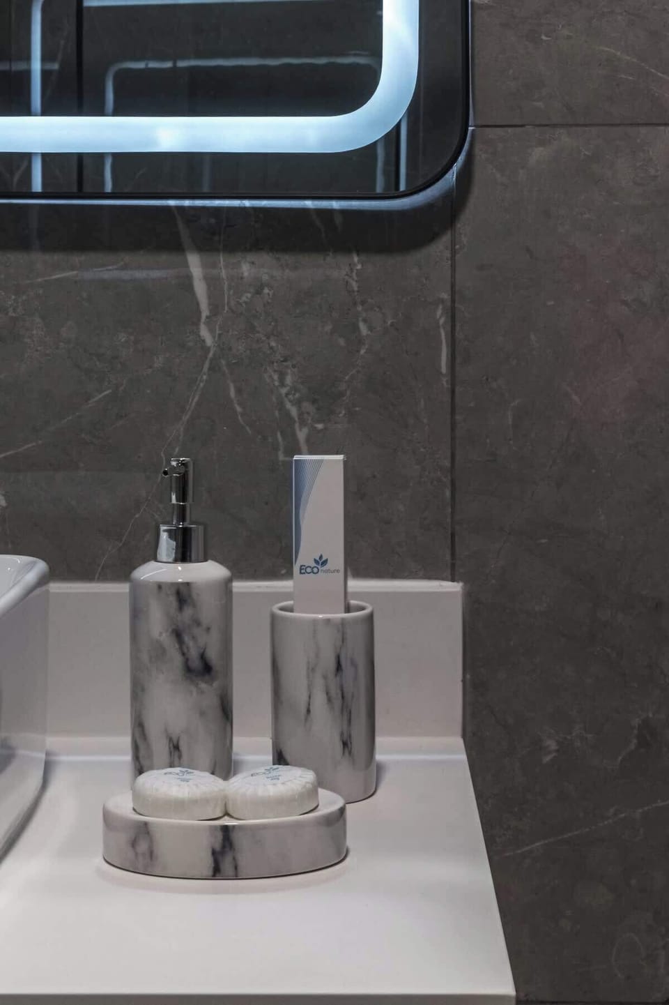 The countertop with marble-inspired accessories and ECO Nature toiletries provides a luxurious and personalized touch.