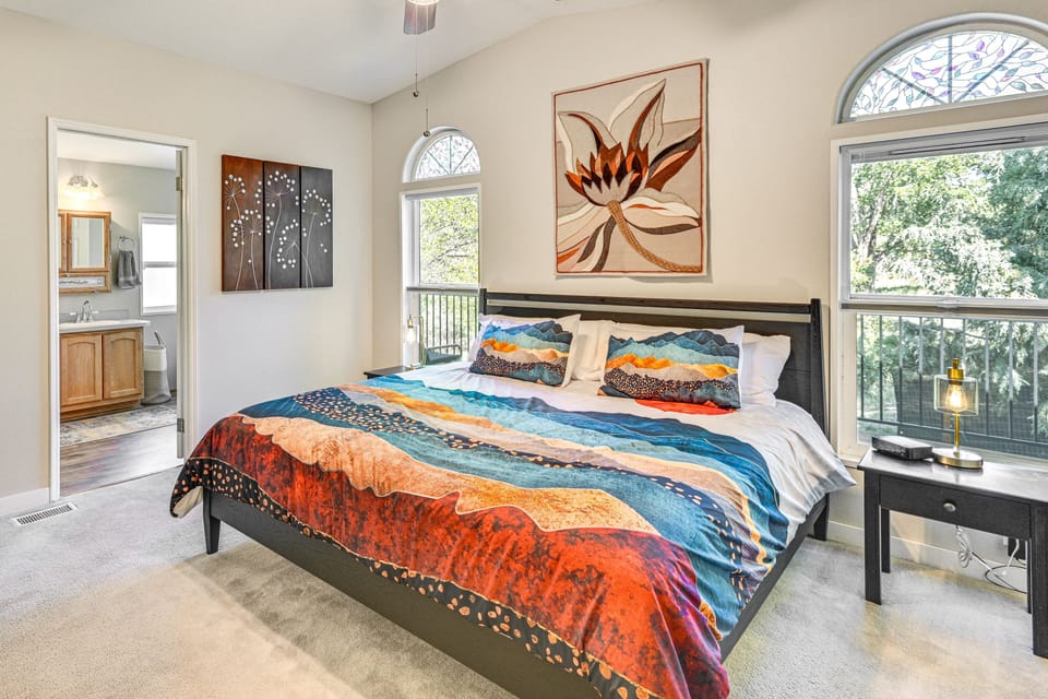 Bedroom with colorful bedding, arched windows, and an adjoining bathroom.