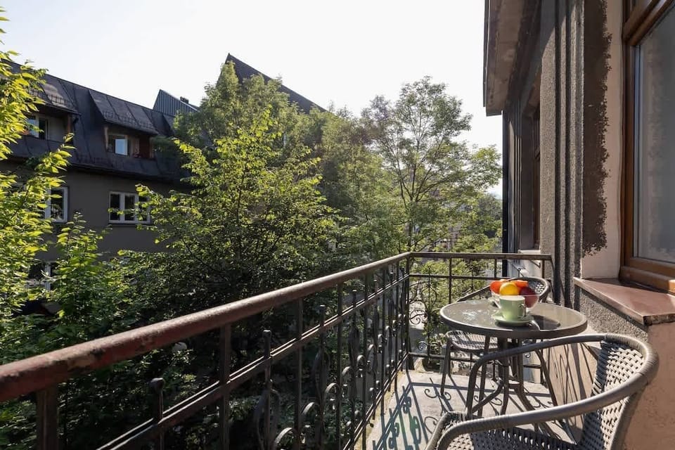 A cozy balcony with a table and chairs, overlooking lush greenery, perfect for enjoying a morning coffee.
