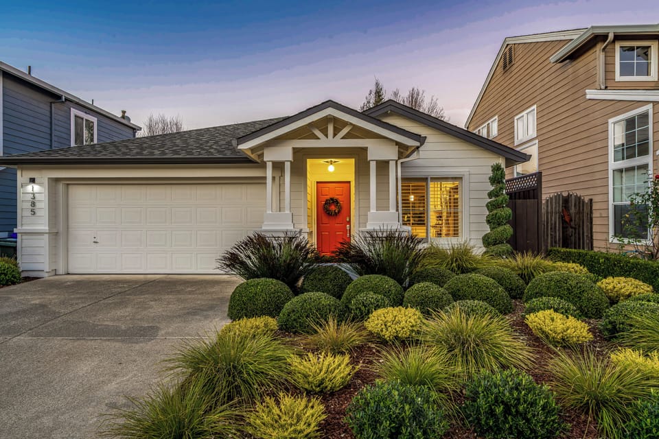 Charming single-story home with vibrant red door and beautifully landscaped front garden in a quiet residential neighborhood.