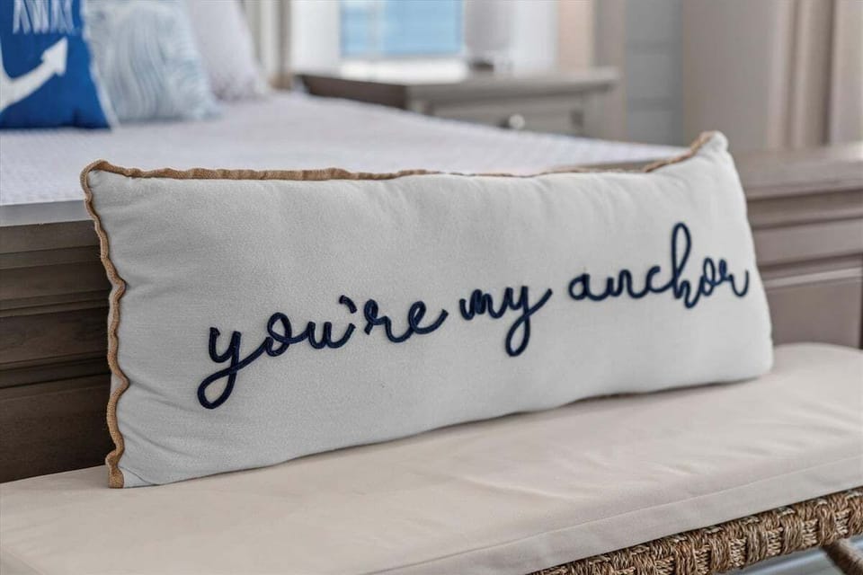 Decorative coastal accent pillow reading “You're my anchor” in the beach themed bedroom.