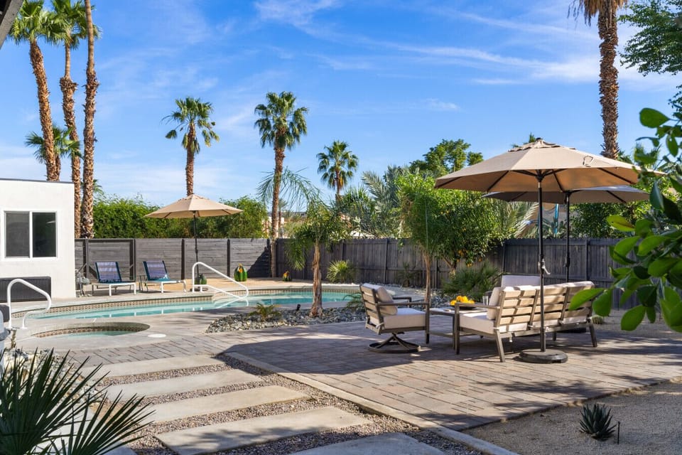 A sunny backyard oasis featuring a pool, palm trees, and a cozy shaded seating area perfect for relaxing outdoors.
