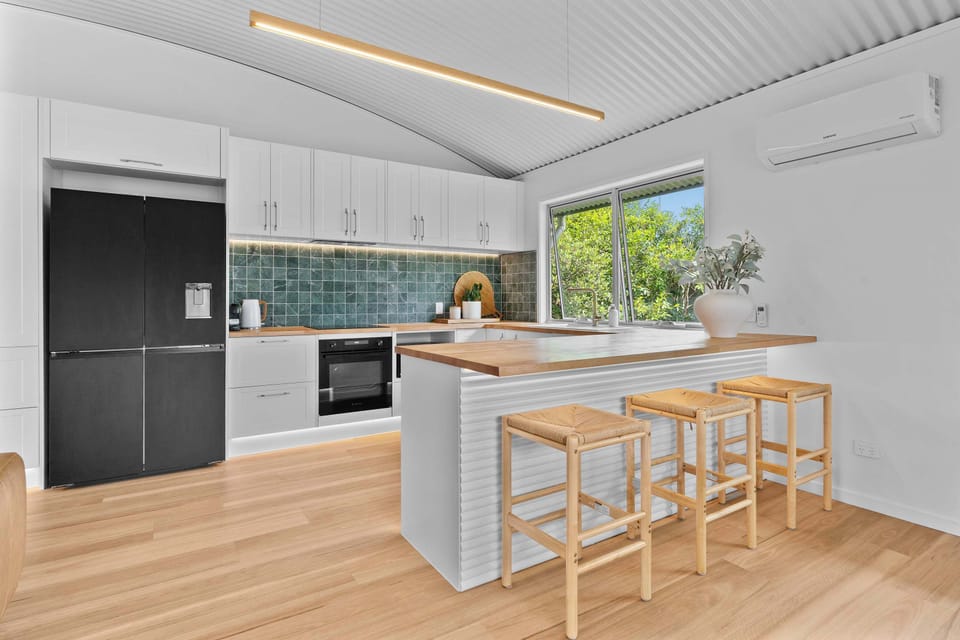 A bright and beautifully styled kitchen with timeless white cabinetry, warm timber finishes, and elegant gold accents ✨ The green tiled backsplash adds a fresh pop of color, creating a space that’s both functional and effortlessly inviting.