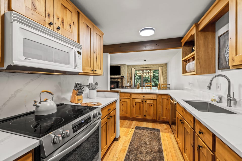 Prepare meals in your fully equipped kitchen with warm wood cabinetry, modern appliances, and bright natural light streaming through windows overlooking the adjacent living space.