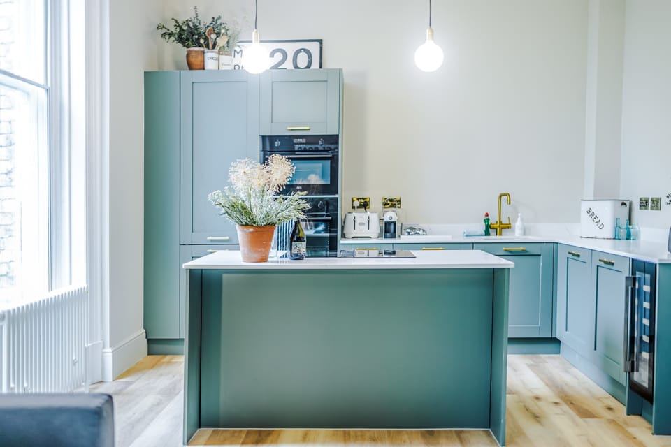 Cook, dine, and unwind in this stunning modern kitchen featuring a spacious island, sleek teal cabinetry, gold accents, and bright open lighting—perfect for family meals or entertaining during your stay. Stylish, spotless, and fully equipped.